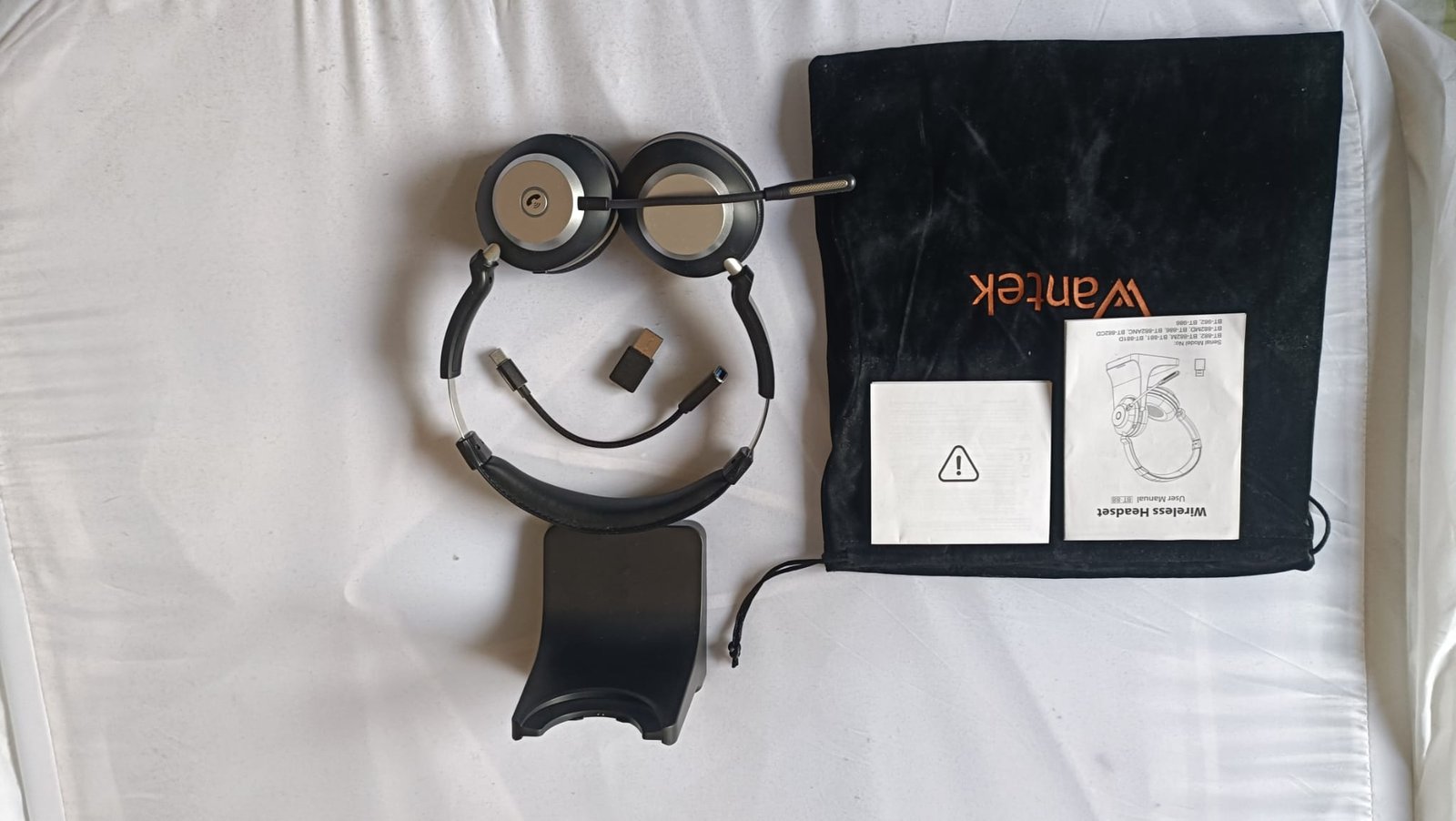 Wantek WK882BT complete accessories flat lay showing headset, charging dock, USB dongle, USB-C adapter, velvet carrying pouch, and user manual