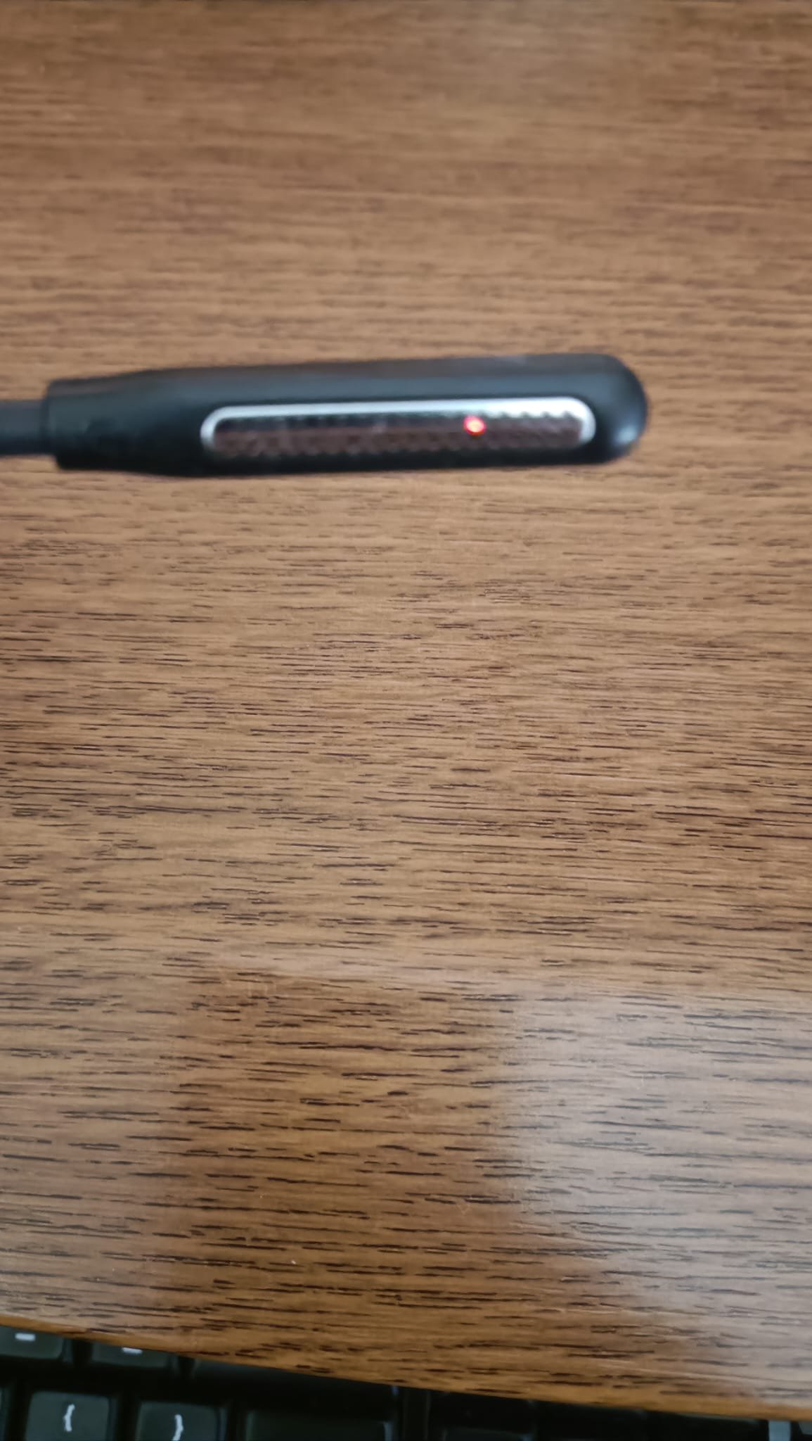 Wantek WK882BT microphone boom tip resting on a desk with the red LED indicator light glowing inside the mic grille, showing mute is active