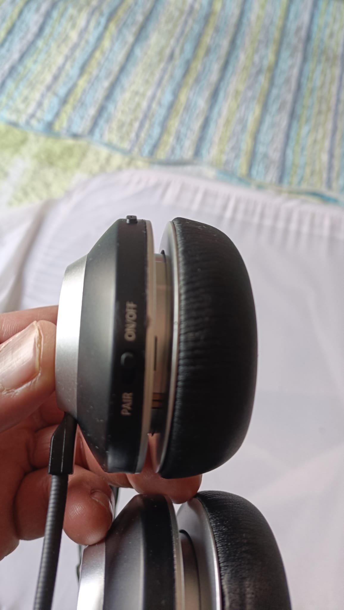 Hand holding the Wantek WK882BT showing the PAIR and ON/OFF slider switch on the edge of the left ear cup