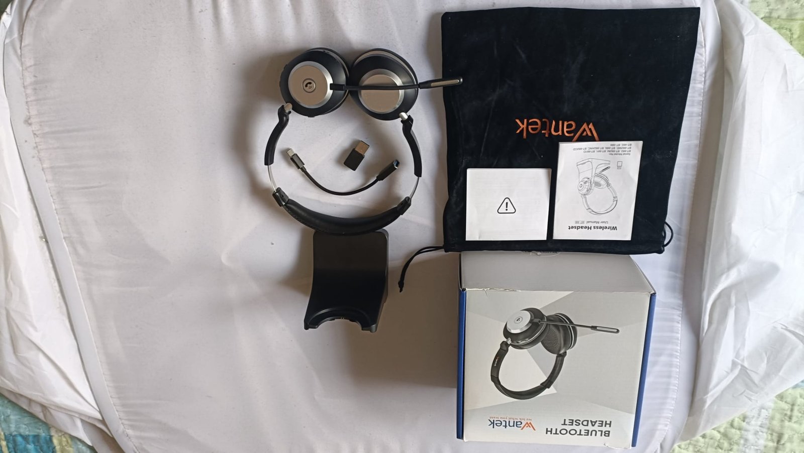 Wantek WK882BT full unboxing flat lay showing headset, USB dongle, USB-C adapter, charging dock, velvet pouch, box, and user manual