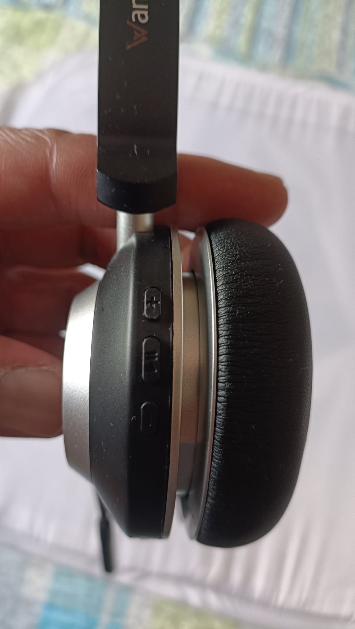 Hand holding the Wantek WK882BT showing three physical buttons on the right ear cup edge: volume up, call/answer, and volume down